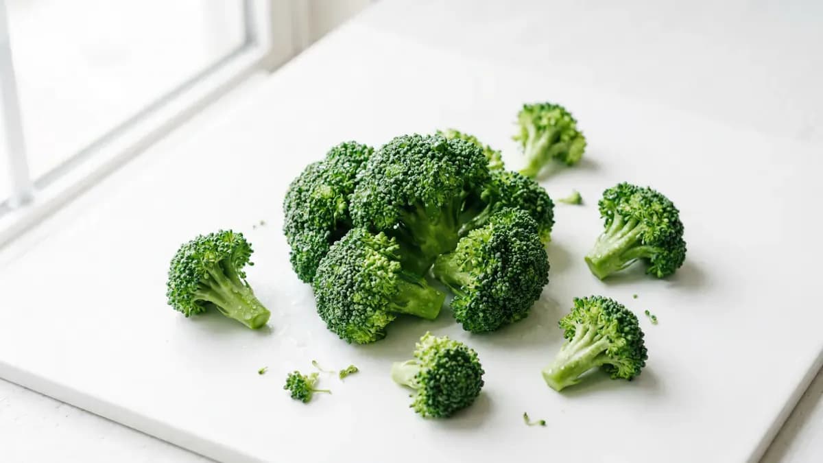 Fresh broccoli florets on a cutting board next to a plate of steamed broccoli ready to serve