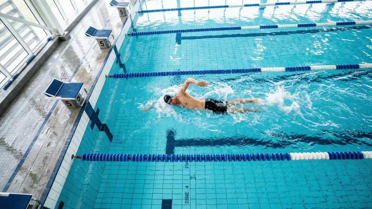 Zwemmer trekt baantjes in een helder verlicht zwembad, bovenaanzicht met blauwe baanlijnen